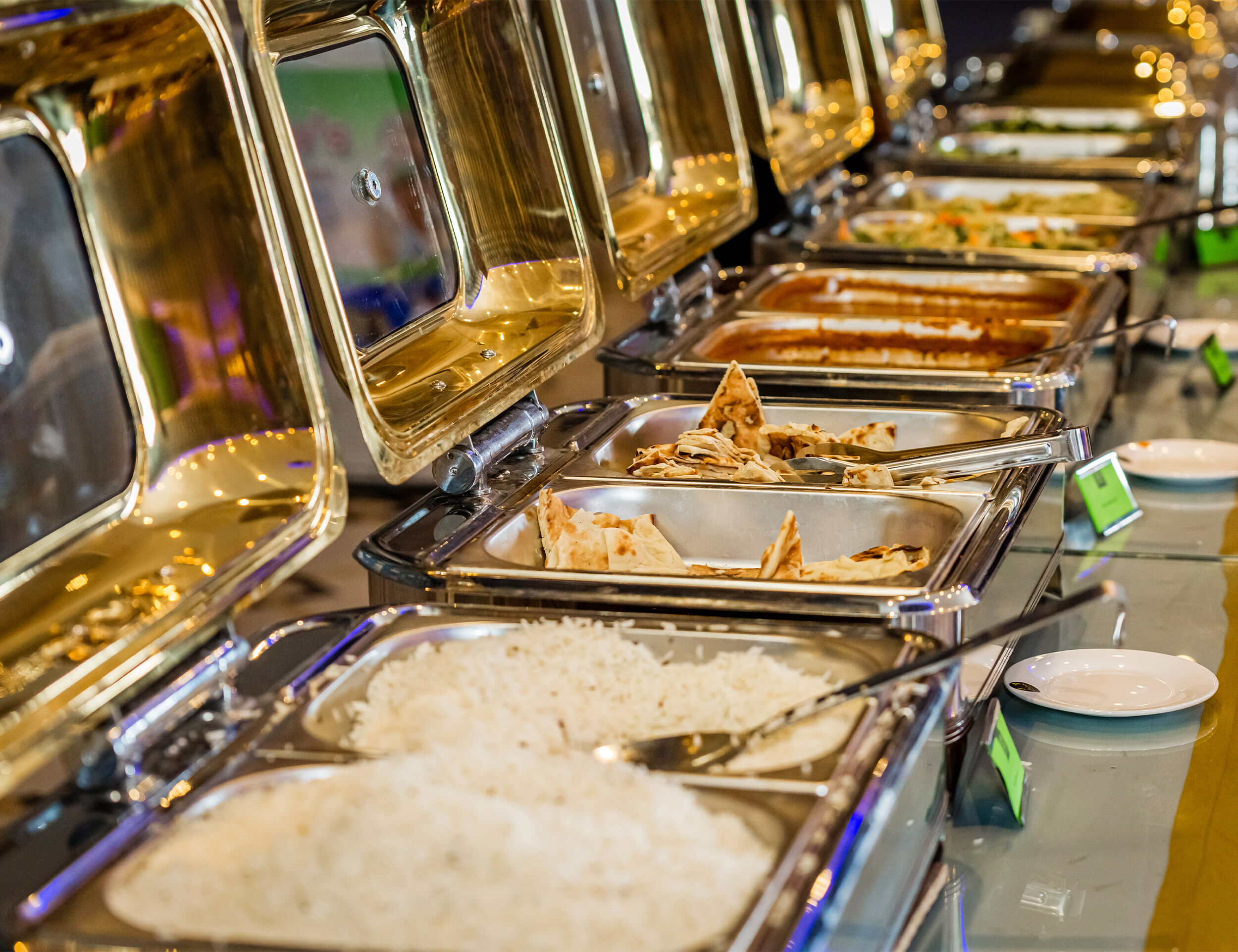 Traditional Indian wedding buffet with naan, rice, curries, and vegetables served in gold-toned chafing dishes.
